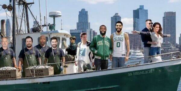 Group of men on a green fishing boat in a harbor, with a city skyline in the background.