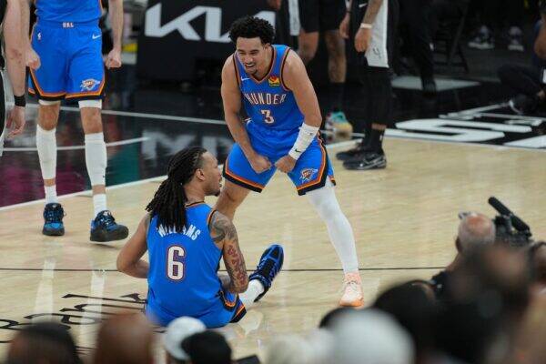 Oklahoma City Thunder players confront each other on the court; one sits on the floor with number 6, the other stands in a ready stance wearing number 3, surrounded by spectators and media.