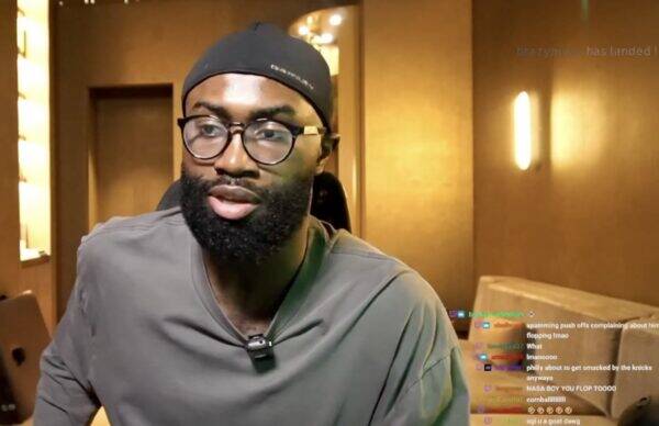 Man with a beard and round glasses speaking to camera in a warmly lit room during a livestream.