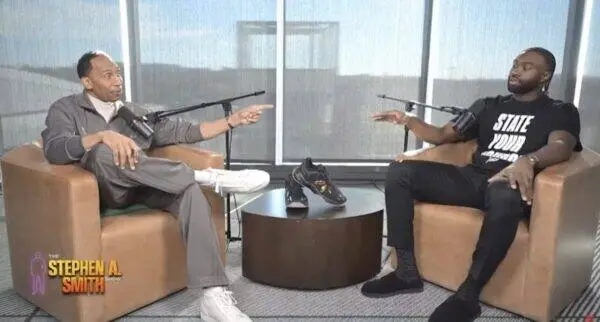 Two men sit in armchairs in a podcast studio, speaking into microphones with sneakers on the table between them, The Stephen A. Smith Show logo visible in the corner.