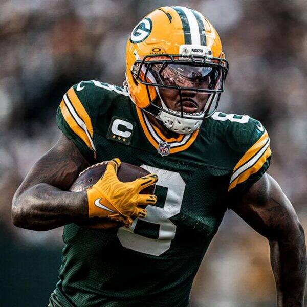 Green Bay Packers running back in green and gold uniform carrying a football during a game with a captain badge on the jersey cap logo visible