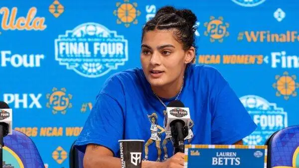 Basketball player Lauren Betts speaks at a press conference microphone with a blue NCAA Final Four backdrop behind her.