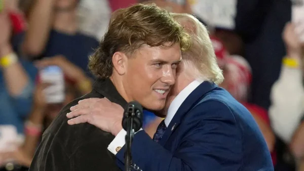 Two men in a close hug on stage, with a microphone in front and a cheering crowd behind them.