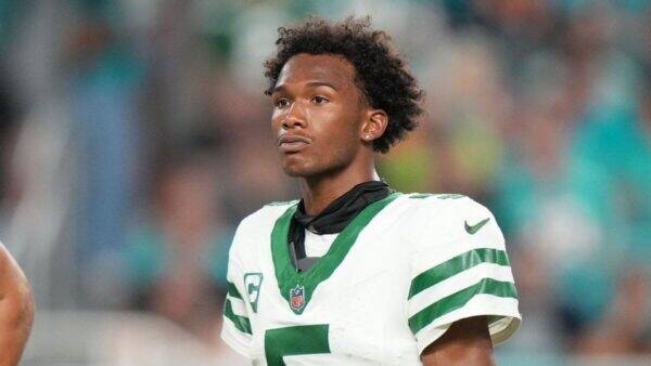 Football player in a white and green jersey with number 7, standing on the field with a focused expression.