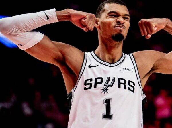 Athlete in a Spurs jersey (number 1) flexing arms during a game, close-up of upper body against dark arena background.