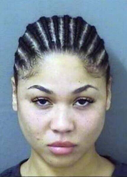 Mugshot-style photo of a young woman with tightly braided hair pulled back, neutral expression, wearing a dark top against a gray background.