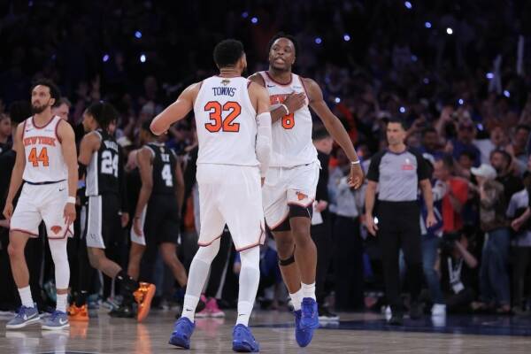 Two basketball players in white uniforms celebrate with a high-five on the court as the crowd cheers behind them.