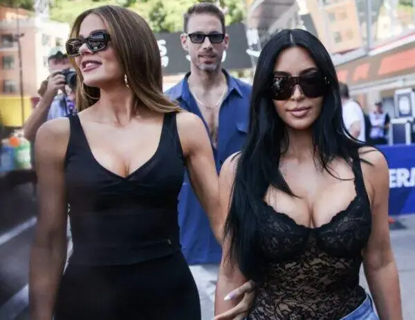 Two women walking together at a sunny outdoor event, both wearing black outfits and dark sunglasses.