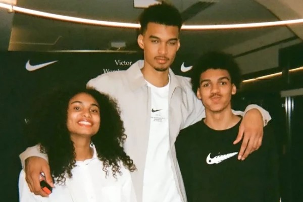 Three young friends posing together with their arms around each other, smiling at the camera, indoors at a Nike event.