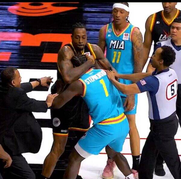 Intense moment on a basketball court as players push and referees separate them during a scuffle.