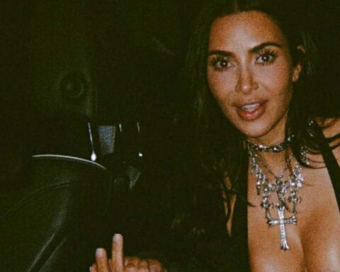 Dimly lit portrait of a woman wearing a plunging neckline and layered silver necklaces with a cross pendant.