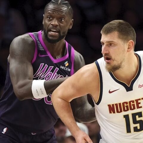 Basketball players in action: Nuggets center wearing white jersey #15 defended by an opponent in a purple uniform during a fast move on the court.
