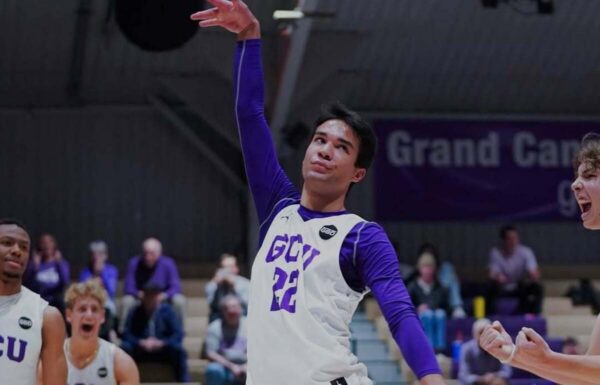 Basketball player in a white jersey with purple sleeves (#22) leaps with arm raised during a game, crowd in the background.