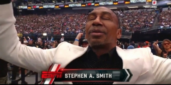 Stephen A. Smith with arms outstretched at a live arena event, wearing a white blazer, with an on-screen banner that reads STEPHEN A. SMITH.