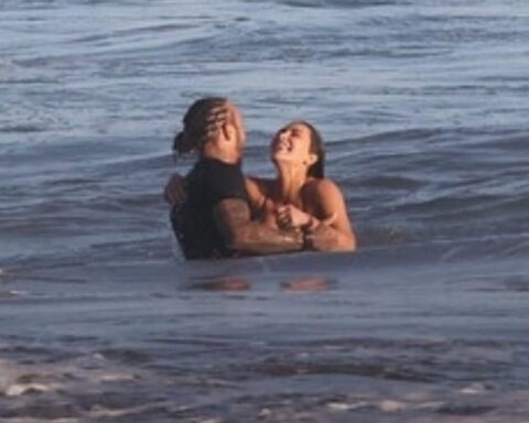 Two people standing waist-deep in the ocean embrace each other in the surf, facing and leaning toward one another.