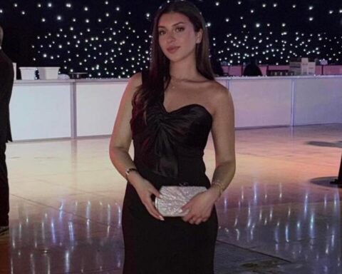 Woman in a strapless black evening gown holding a silver clutch at a formal event on a lit dance floor.