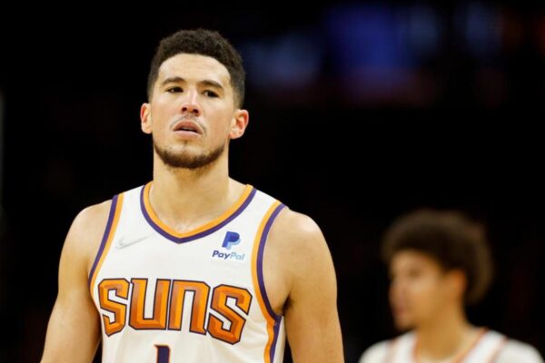 Male basketball player wearing a Phoenix Suns jersey on a court, looking upward in focus.