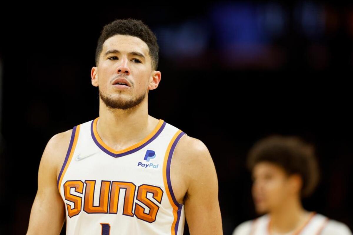 Male basketball player wearing a Phoenix Suns jersey on a court, looking upward in focus.