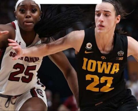 Two female college basketball players sprint toward the ball; Iowa player #22 in black drives while South Carolina player #25 in white defends.