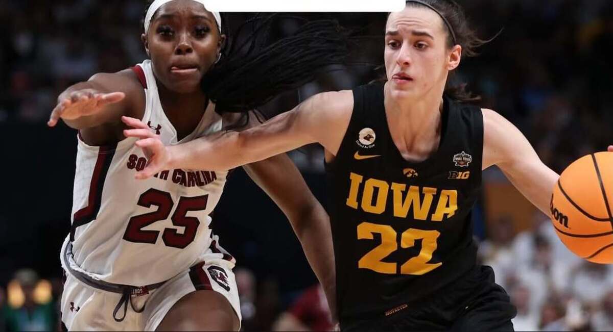 Two female college basketball players sprint toward the ball; Iowa player #22 in black drives while South Carolina player #25 in white defends.