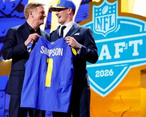 Two men in suits on stage hold up a blue jersey that reads 'Simpson' with the number 1 at the 2026 NFL Draft event.