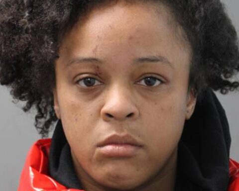 Mugshot of a young woman with curly hair, wearing a red jacket, facing the camera with a neutral expression.