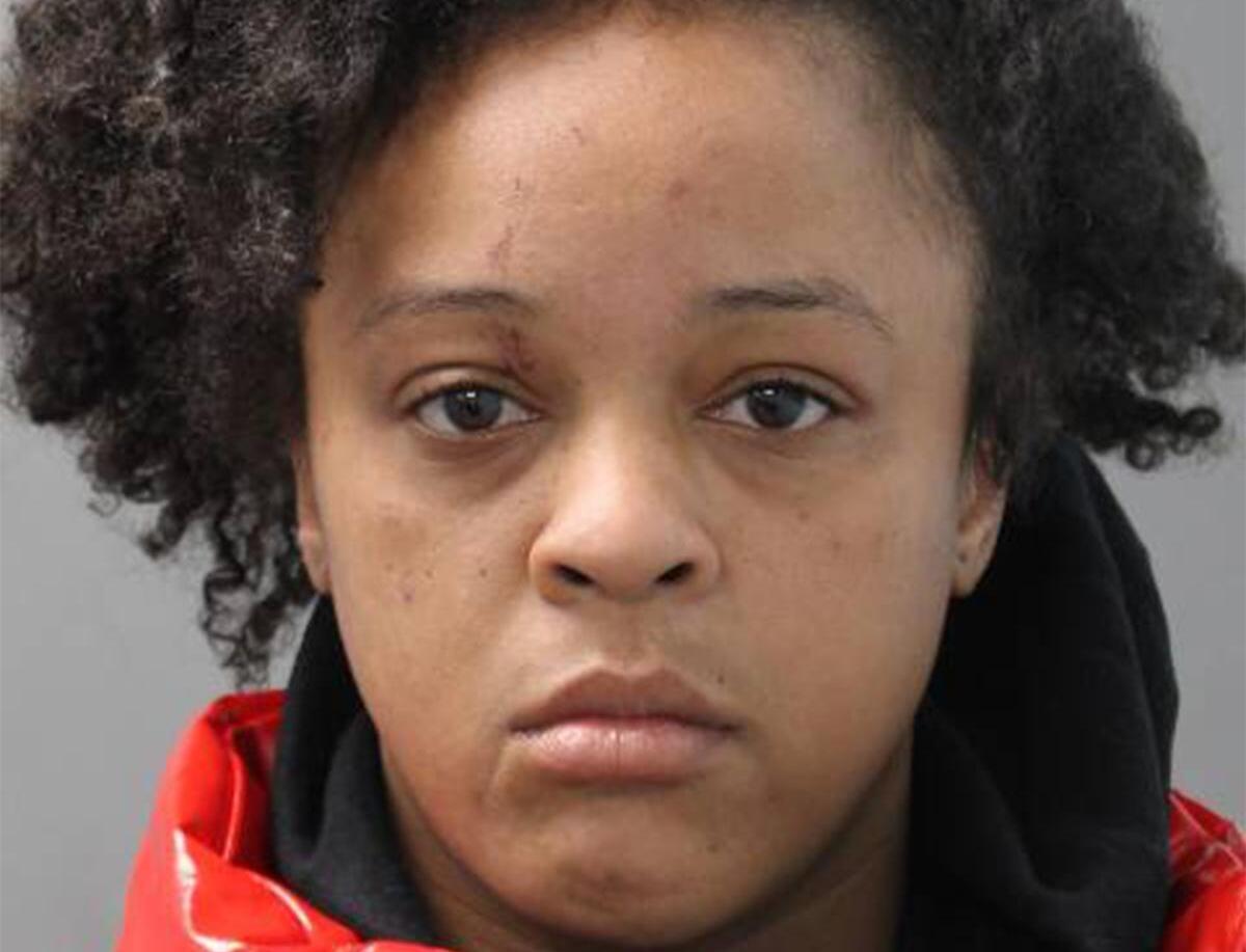 Mugshot of a young woman with curly hair, wearing a red jacket, facing the camera with a neutral expression.