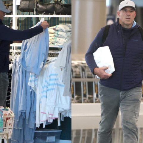 Two men in navy vests shop: left man selects light-blue jackets from a rack; right man walks carrying a white paper bag.