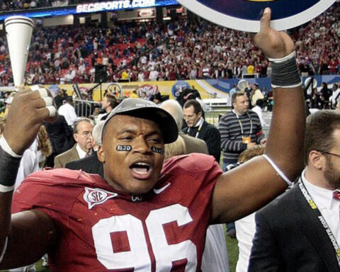 Football player in red jersey raises trophy above his head amid a stadium celebration, fans in the background