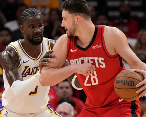 Rockets guard in red drives with the ball as a Lakers defender in white and purple closely guards him.
