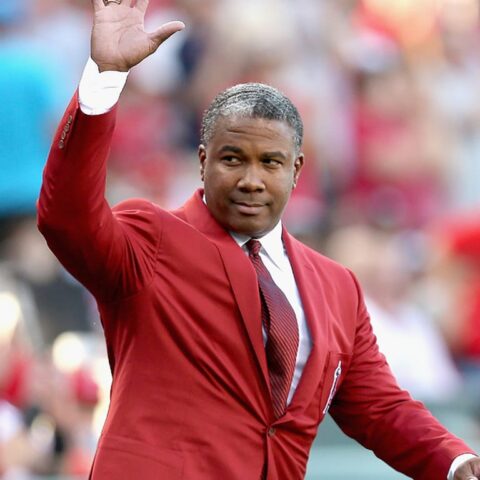 Man in a red suit waving to a cheering crowd at a stadium