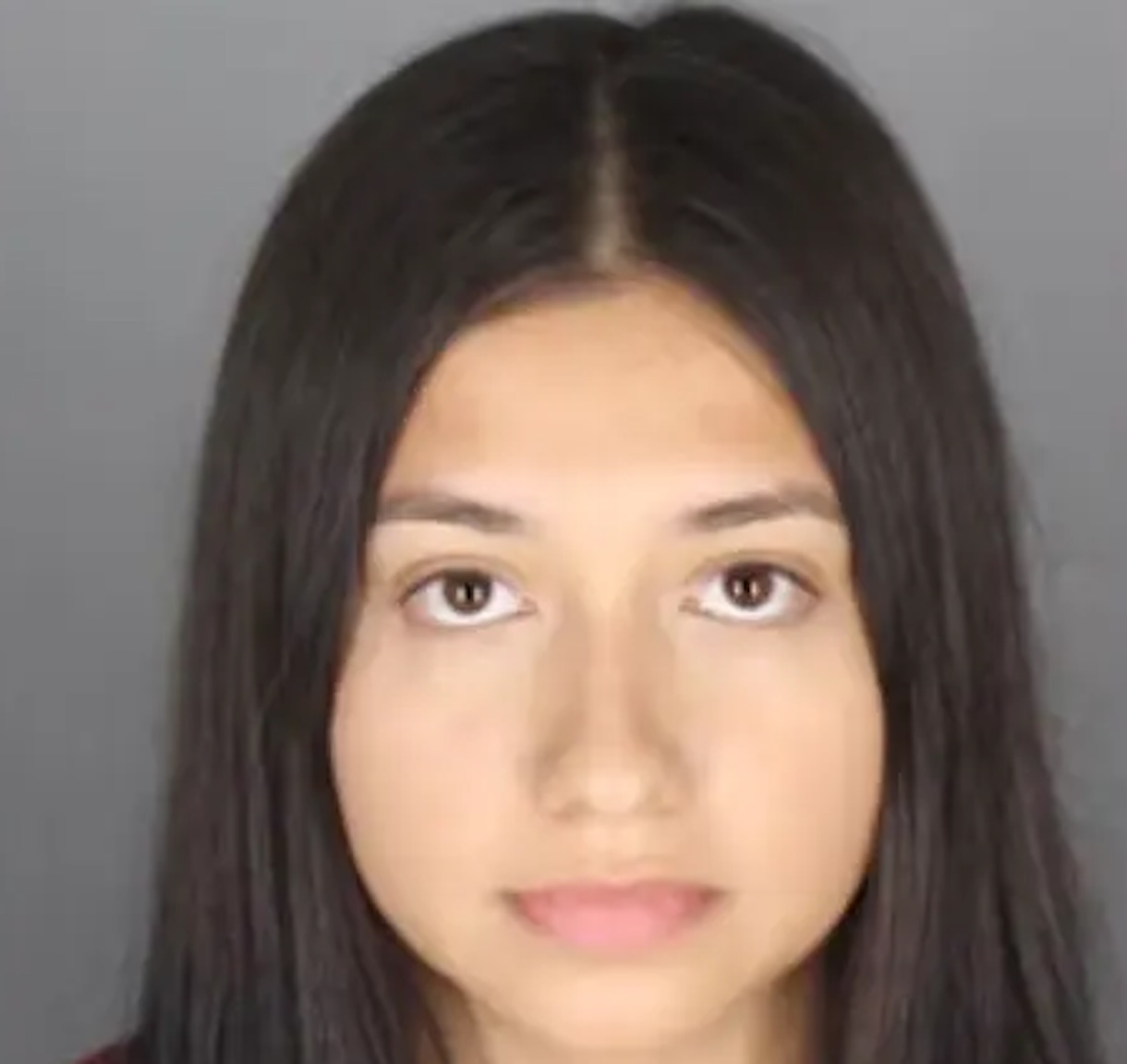 Close-up portrait of a young woman with long dark hair and neutral expression against a gray background.