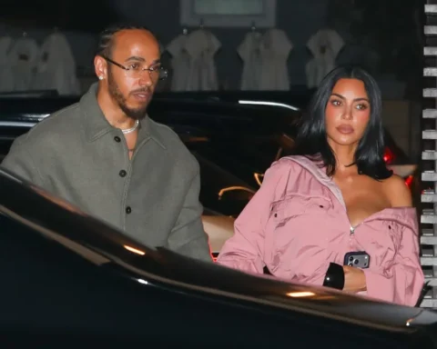 A man and a woman exit a dark car at night; the woman wears a pink off‑shoulder jacket and holds a phone, the man wears a gray coat and glasses.