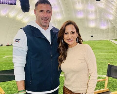 Smiling man and woman pose together inside a large indoor sports facility with artificial turf under a dome.