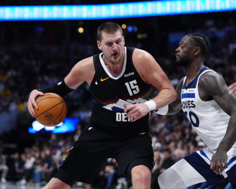 Two basketball players sprint on the court; black jersey #15 drives with the ball while a defender in a white Wolves jersey pursues him.