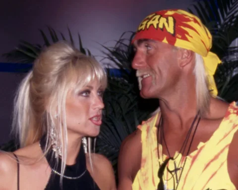Two adults facing each other and smiling at a tropical-themed party, woman in black dress and earrings, man in yellow-red bandana and tie-dye outfit.