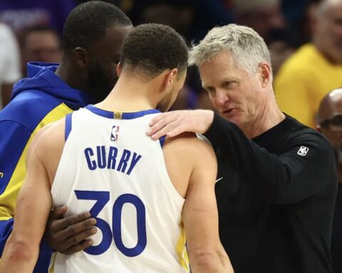 Basketball coach places a hand on a player's shoulder during a timeout, a white jersey with the number 30 visible.