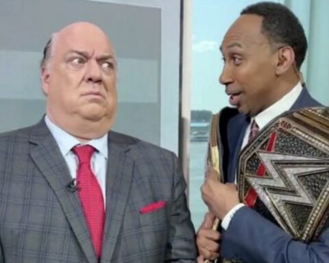 Two men in suits indoors; the left man frowns as the right man shows a large championship belt.