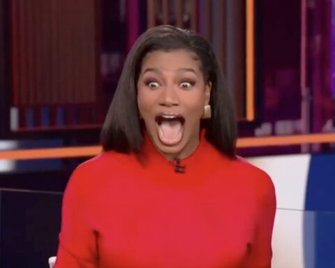 Woman in a red top on a TV set, mouth wide open in surprised/excited expression.