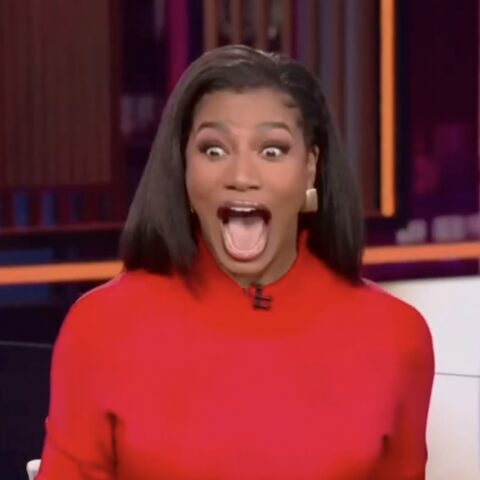 Woman in a red top on a TV set, mouth wide open in surprised/excited expression.