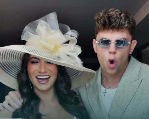 Woman wearing a large striped sun hat with a flower, smiling beside a man in a light blazer and sunglasses making a surprised expression.
