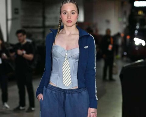 Model walking backstage in a blue tracksuit with a corset-style light blue top and striped tie.