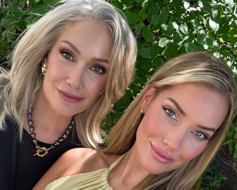 Two women posing for a close-up selfie outdoors with green foliage in the background, smiling softly.