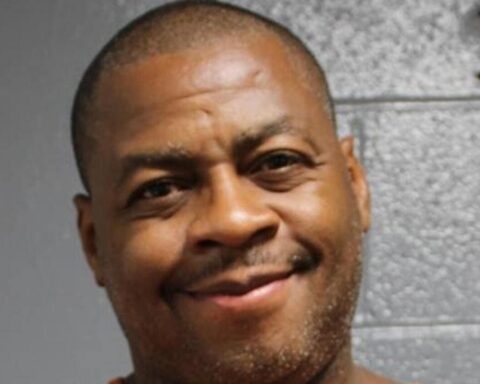 Close-up portrait of a smiling man with short hair against a gray wall background.