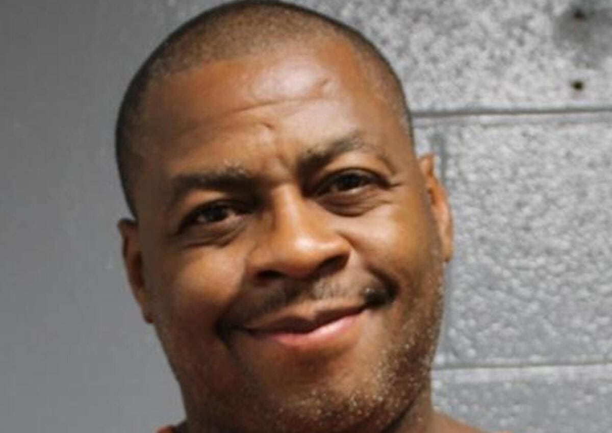 Close-up portrait of a smiling man with short hair against a gray wall background.