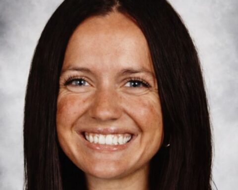 Smiling woman with long dark hair against a gray studio backdrop.