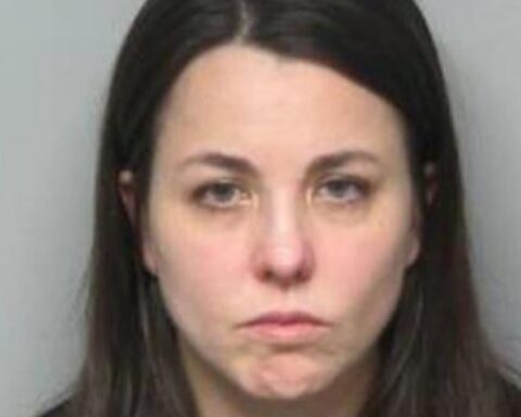 Front-facing mugshot of a woman with long dark hair and a neutral, solemn expression against a gray background.