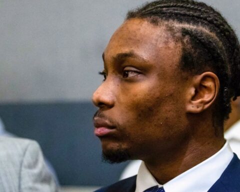 Side profile of a Black man in a navy suit, white shirt, looking toward the left in a formal setting.