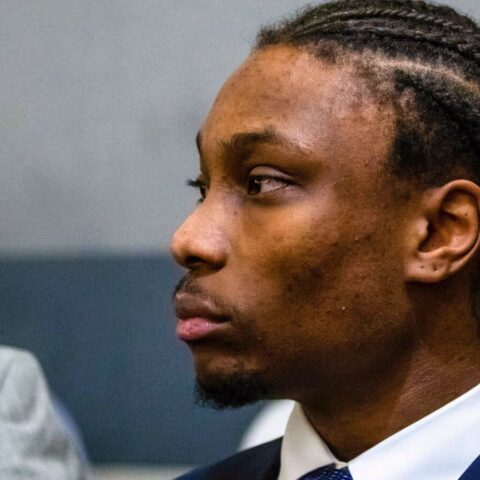 Side profile of a Black man in a navy suit, white shirt, looking toward the left in a formal setting.