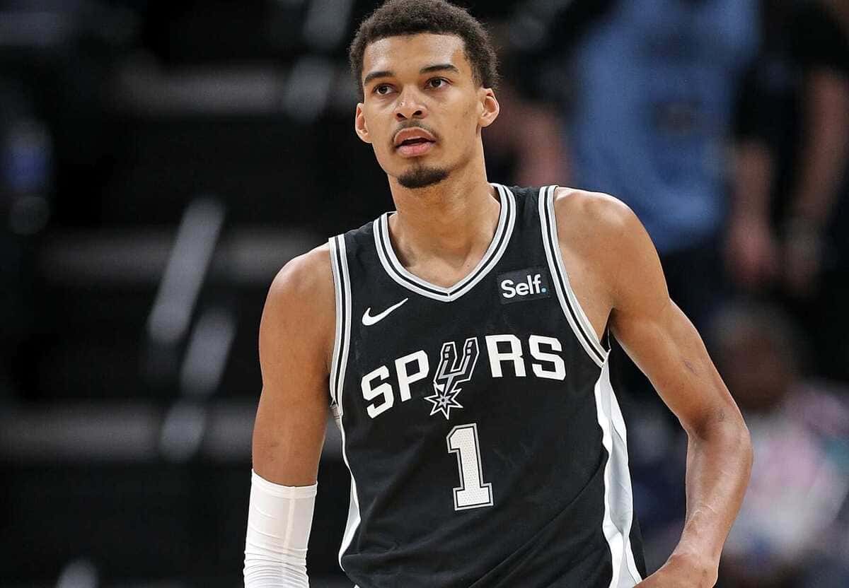 Basketball player in a Spurs black jersey with number 1, standing on the court during a game, looking ahead.